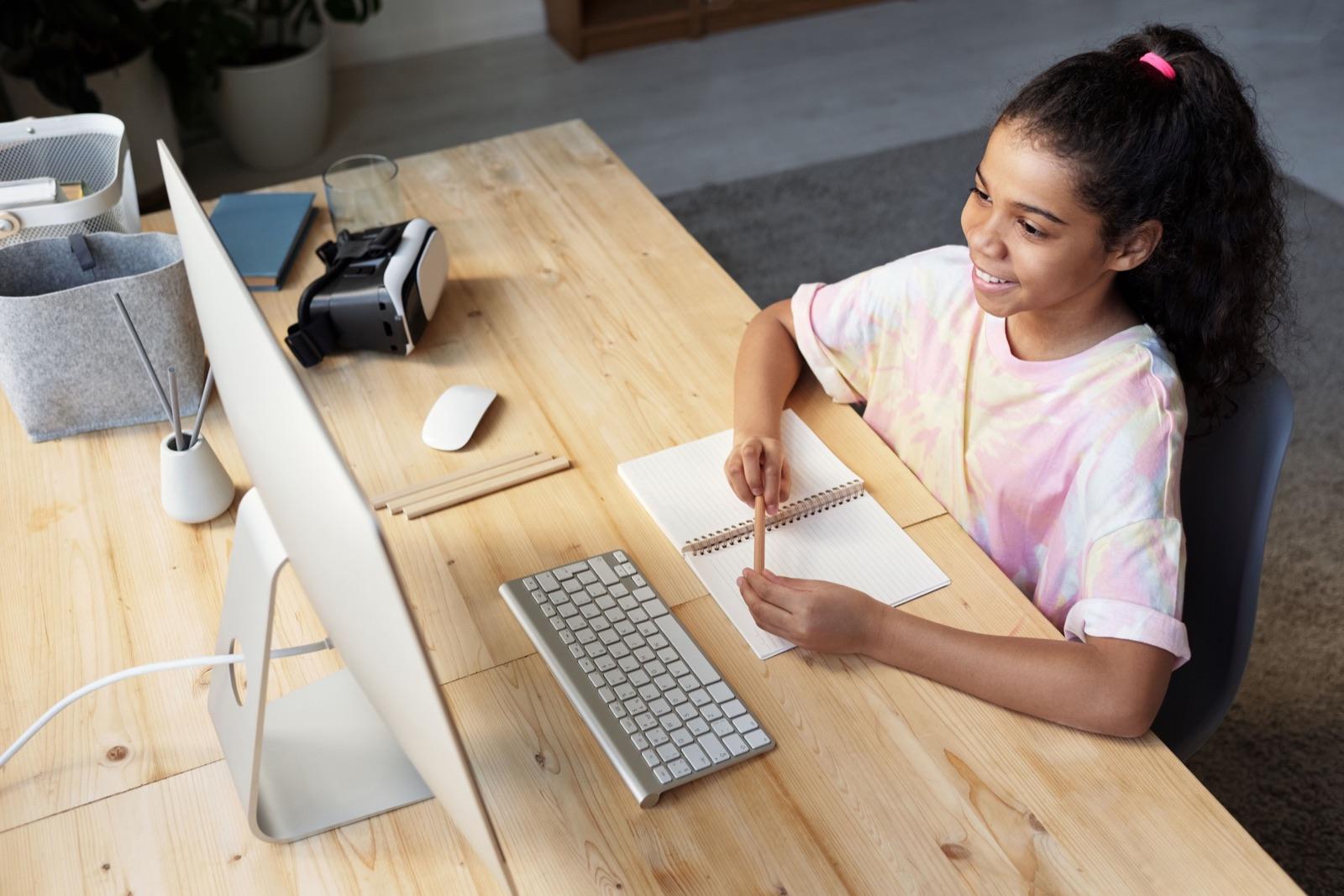 An older teenager working at a desktop computer with a notebook